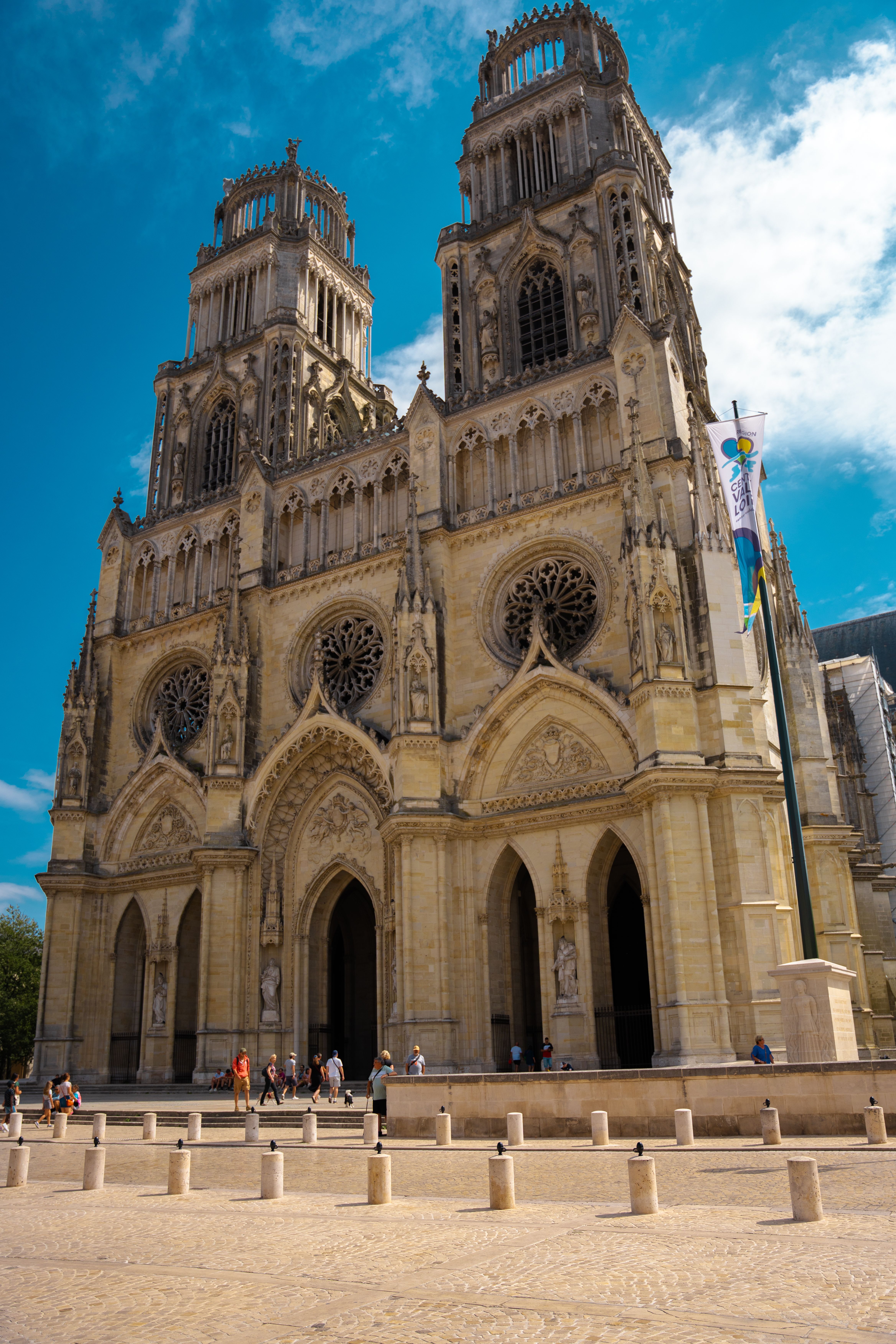 Facade gothique de cathédrale majestueuse sous ciel bleu, visiteurs devant l’entrée principale, grande porte et vitraux volumineux.